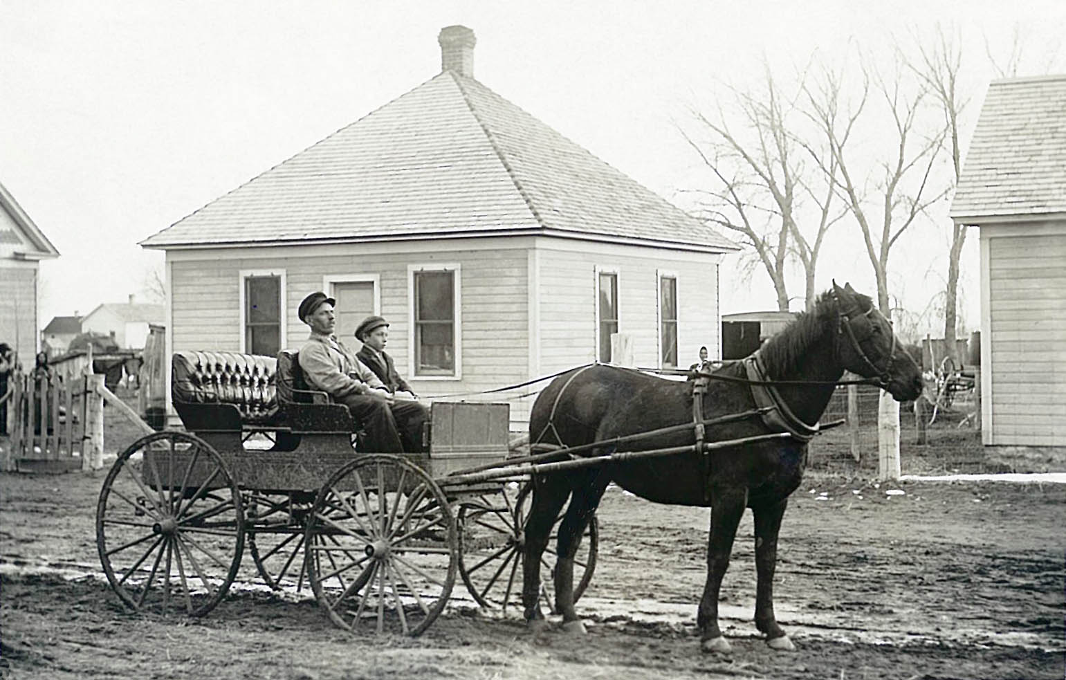 Black and white photograph of a man and younger boy sitting in a horse drawn cart.